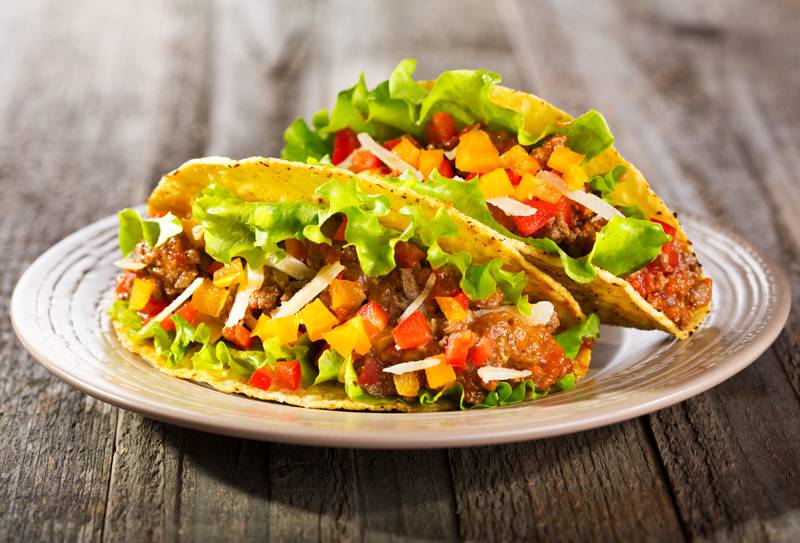 A close up shot of two well-filled tacos on a plate that is on a wooden table.