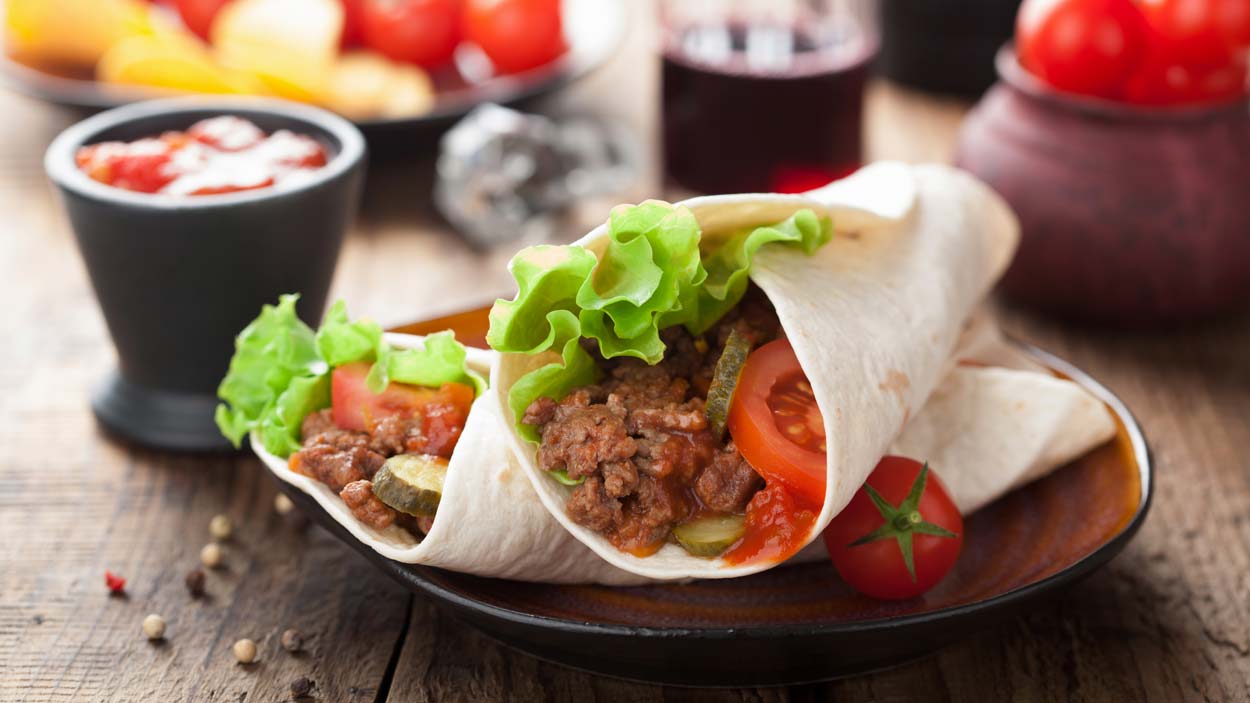 Tortilla wraps or burritos on a plate that is on a wooden table with some condiments in the background