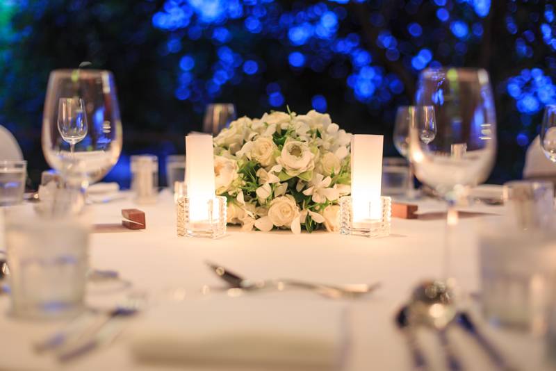 Close up picture of a wedding or quinceañera table with flowers in the middle, glasses, silverware, and napkins. Blurred background with blue LED lights.